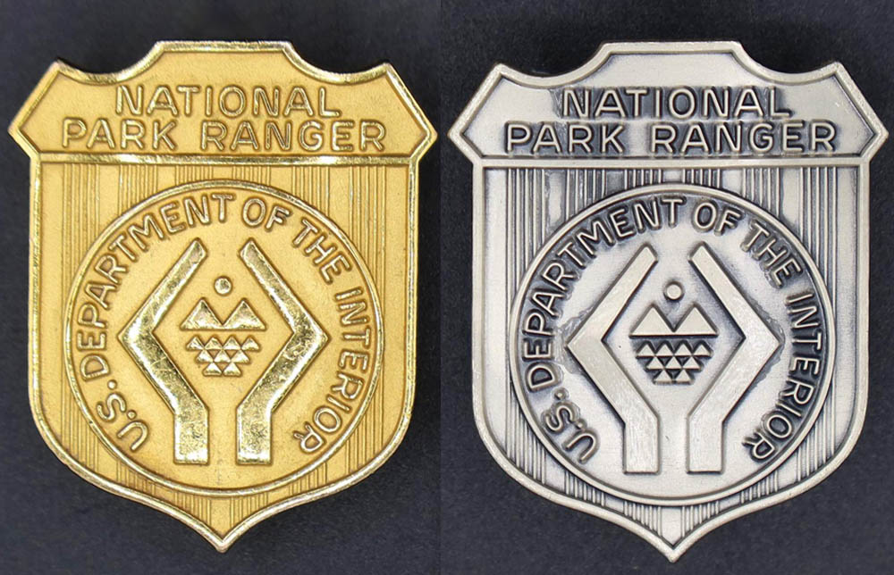 A gold and a silver badge marked National Park Ranger. The round seal in the middle has a stylized pair of hands cupping a sun, mountains, and water.